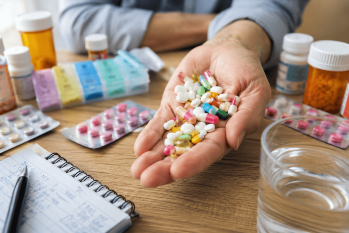 Patient holding multiple prescription pills beside medication bottles and a pill organizer, illustrating the challenges of polypharmacy and medication burden.